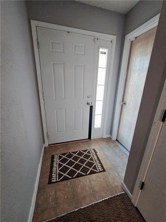 tiled entryway with a textured wall and baseboards