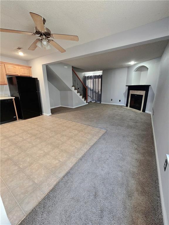 unfurnished living room featuring a textured ceiling, a fireplace, baseboards, light colored carpet, and stairs