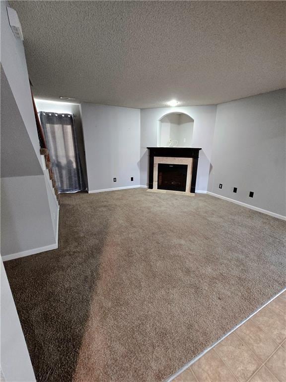 unfurnished living room with a fireplace with flush hearth, light colored carpet, a textured ceiling, and baseboards