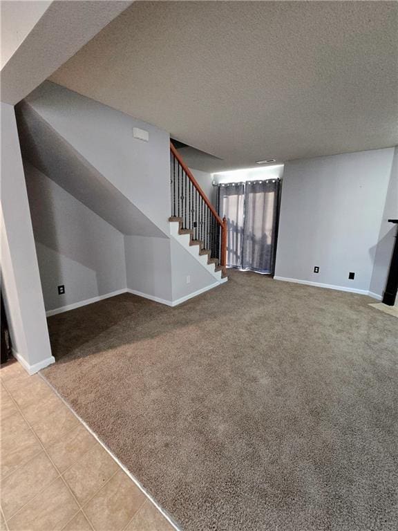 unfurnished living room with a textured ceiling, carpet, tile patterned flooring, baseboards, and stairs