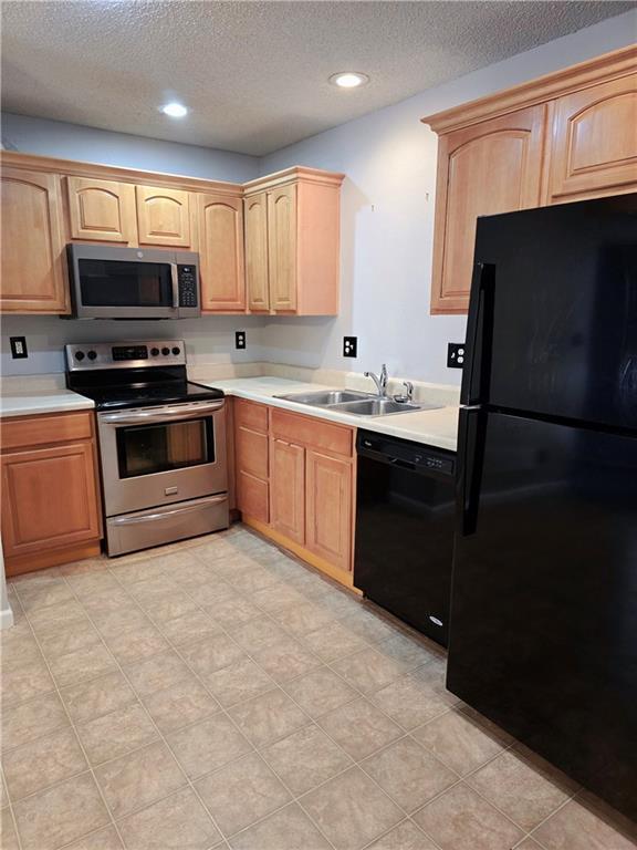 kitchen with light brown cabinetry, black appliances, light countertops, and a sink