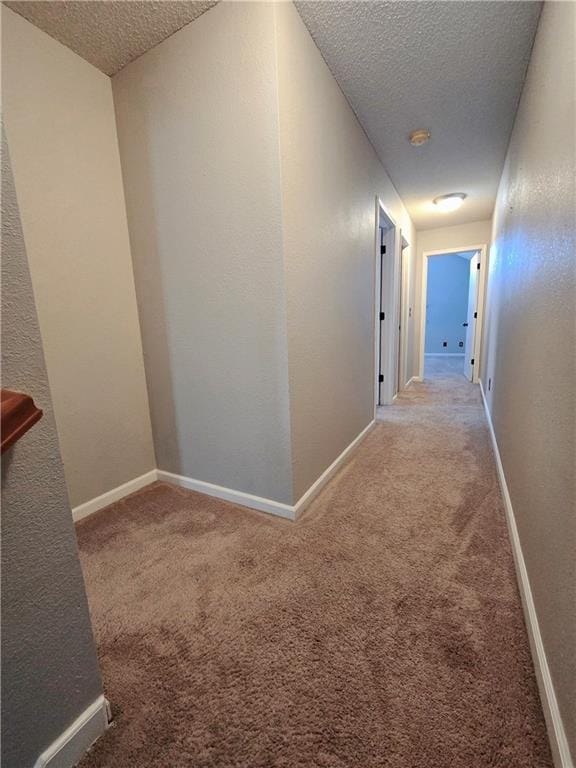 corridor featuring baseboards, a textured ceiling, and carpet flooring