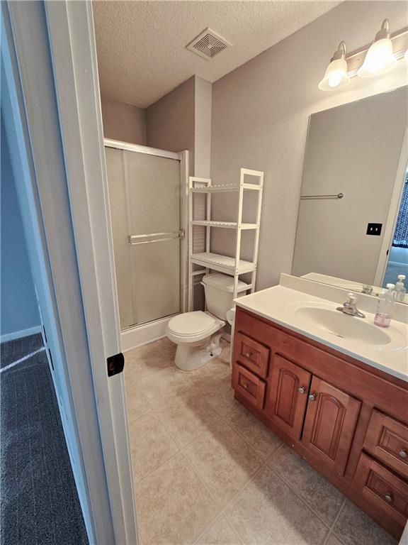 bathroom with a shower stall, toilet, visible vents, and a textured ceiling