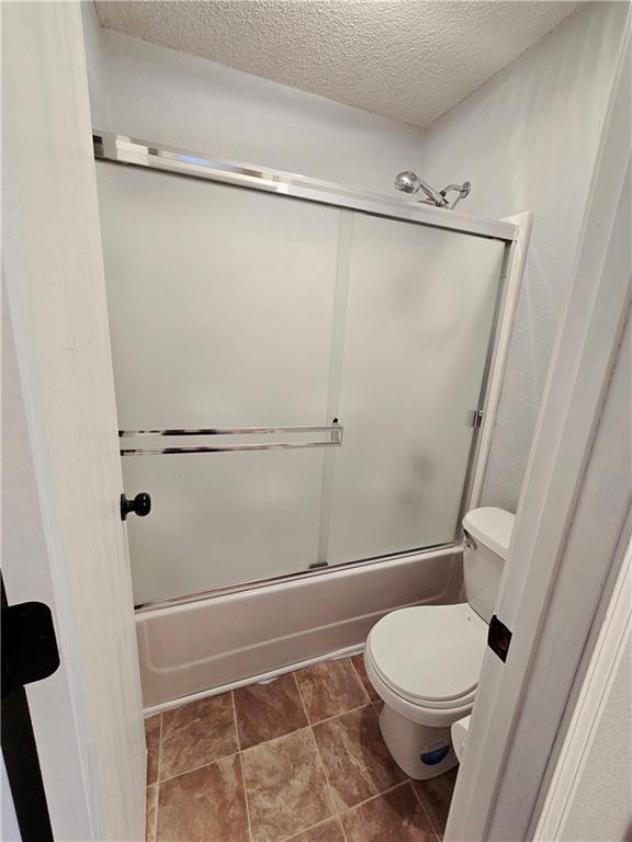 bathroom featuring enclosed tub / shower combo, toilet, and a textured ceiling