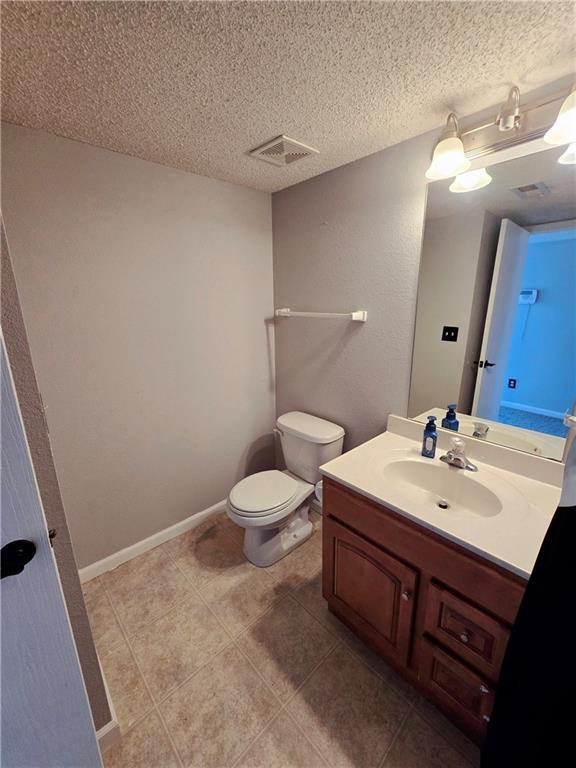 bathroom with visible vents, toilet, a textured ceiling, baseboards, and vanity