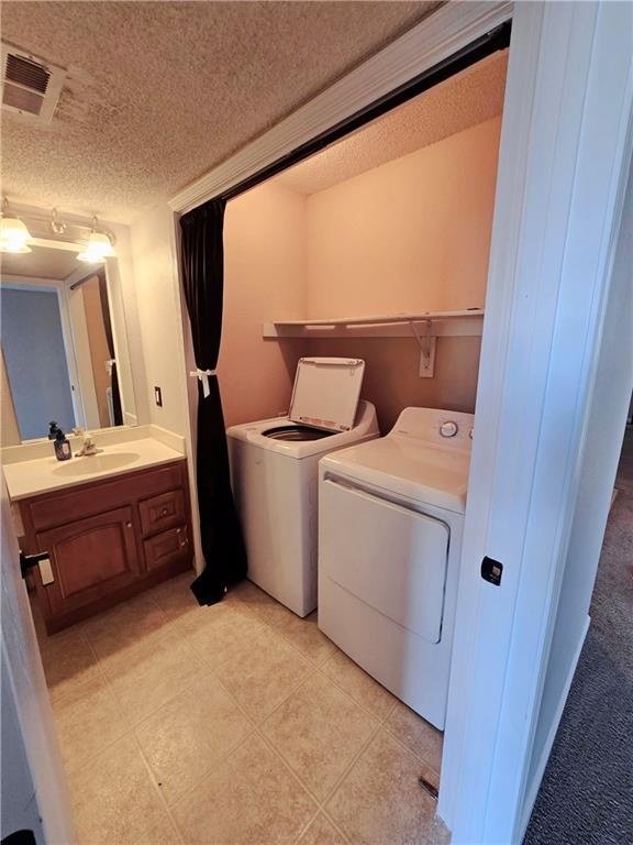 laundry area featuring visible vents, laundry area, a sink, a textured ceiling, and independent washer and dryer