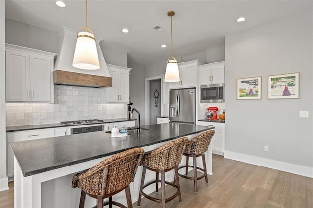 kitchen with stainless steel appliances, visible vents, white cabinets, and an island with sink