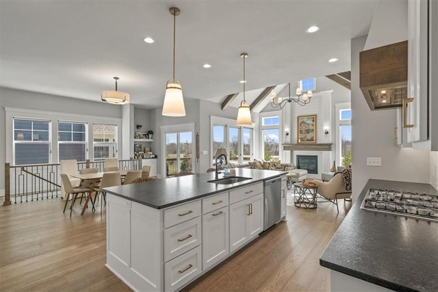 kitchen with a sink, light wood-style floors, appliances with stainless steel finishes, dark countertops, and open floor plan