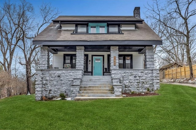 view of front of house with a chimney, covered porch, a front yard, and fence