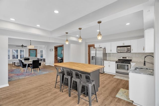 kitchen featuring a kitchen bar, stainless steel appliances, light wood-style floors, white cabinetry, and a sink