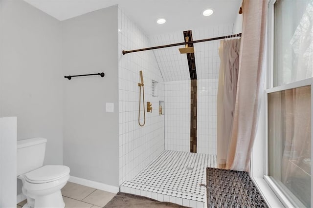 bathroom featuring tile patterned floors, a tile shower, toilet, and baseboards