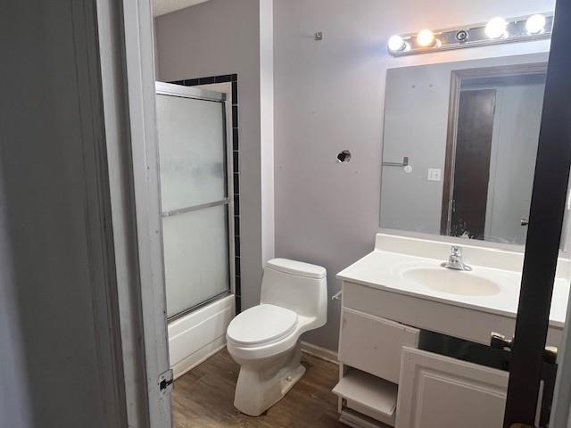 full bathroom with bath / shower combo with glass door, toilet, vanity, and wood finished floors