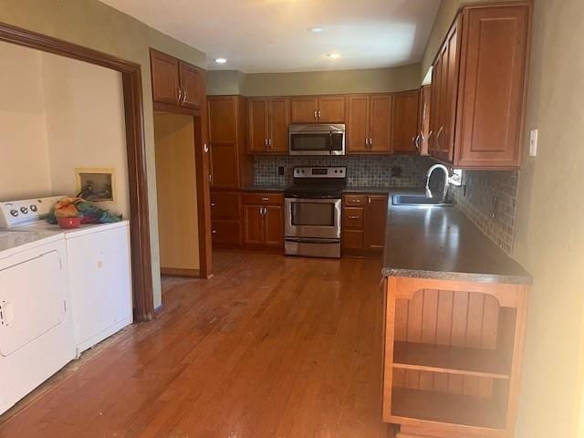 kitchen with wood finished floors, a sink, stainless steel appliances, brown cabinets, and washer and clothes dryer