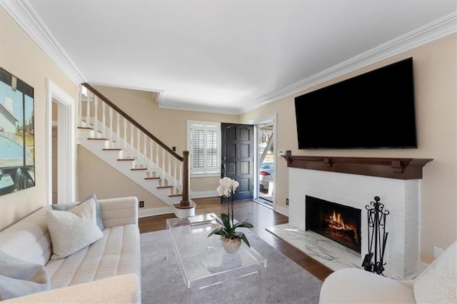 living area with stairs, ornamental molding, wood finished floors, and a lit fireplace