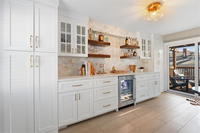 bar featuring backsplash, a bar, beverage cooler, and light wood finished floors