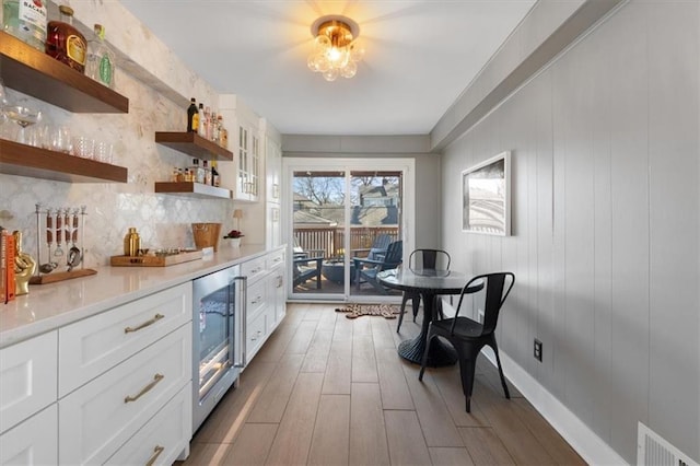 kitchen with open shelves, wood finished floors, wine cooler, white cabinets, and decorative backsplash