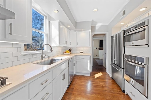 kitchen with a sink, white cabinets, wall chimney exhaust hood, and stainless steel appliances