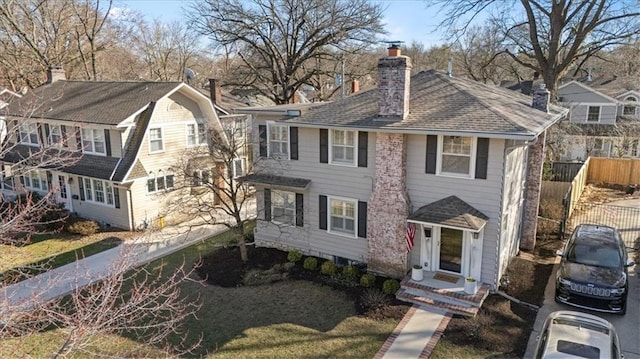 view of front of house featuring a gambrel roof, roof with shingles, a chimney, and fence