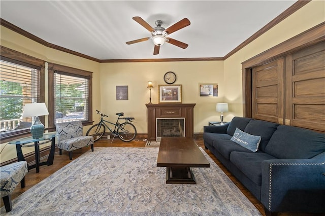 living room featuring wood finished floors, a ceiling fan, baseboards, a fireplace, and crown molding