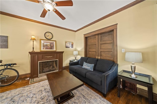 living area featuring baseboards, ornamental molding, a fireplace, wood finished floors, and a ceiling fan