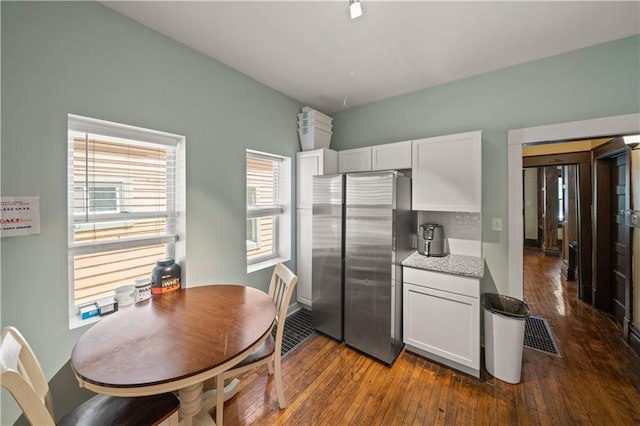 kitchen with light stone countertops, visible vents, freestanding refrigerator, dark wood-type flooring, and white cabinetry