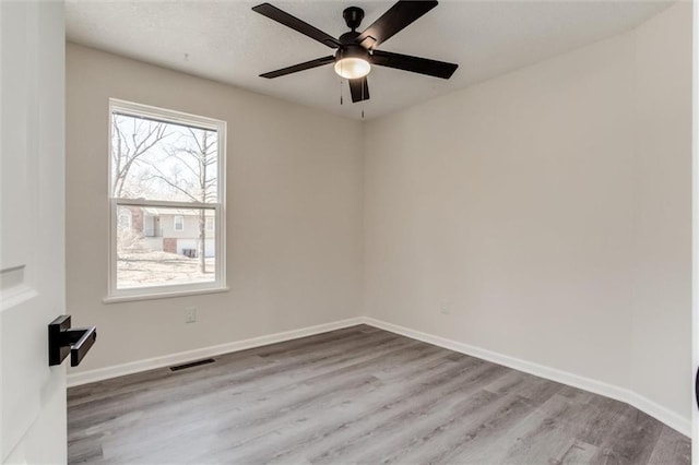 unfurnished room with a ceiling fan, wood finished floors, visible vents, and baseboards