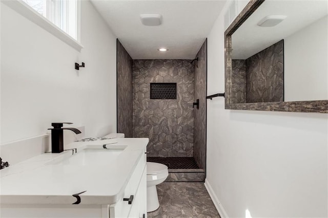 bathroom with vanity, toilet, baseboards, and tiled shower