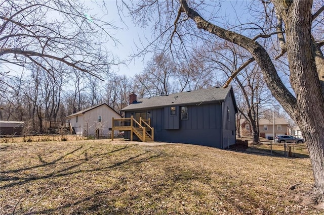 back of property with a chimney, fence, a yard, board and batten siding, and stairs