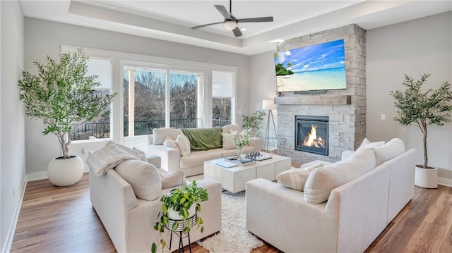 living room with baseboards, ceiling fan, a fireplace, wood finished floors, and a raised ceiling