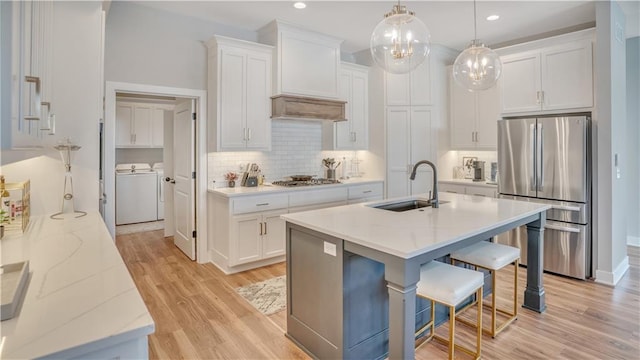 kitchen with light wood-type flooring, a sink, washer and dryer, appliances with stainless steel finishes, and white cabinets