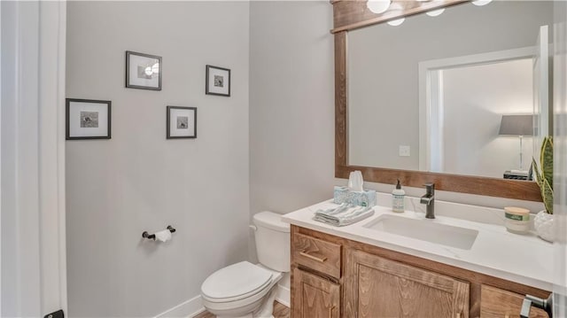 half bath featuring baseboards, toilet, and vanity