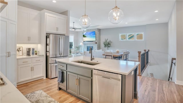 kitchen with a fireplace, a sink, stainless steel appliances, white cabinets, and light wood-type flooring