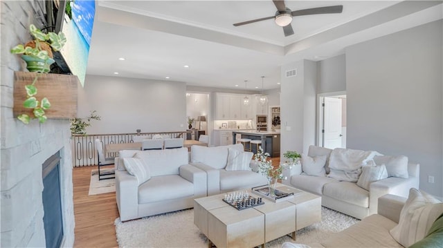 living room featuring light wood-type flooring, a ceiling fan, recessed lighting, a fireplace, and a raised ceiling