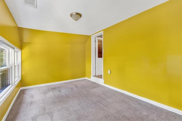 carpeted spare room with visible vents, lofted ceiling, and baseboards