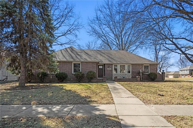 view of front of home with brick siding, a front yard, and a shingled roof