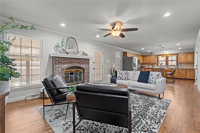 living room with visible vents, a brick fireplace, crown molding, baseboards, and light wood-style flooring