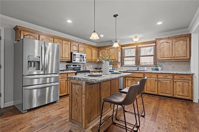 kitchen with appliances with stainless steel finishes, a kitchen island, dark wood-type flooring, and ornamental molding