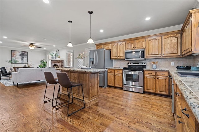 kitchen with wood finished floors, a breakfast bar, decorative backsplash, appliances with stainless steel finishes, and open floor plan