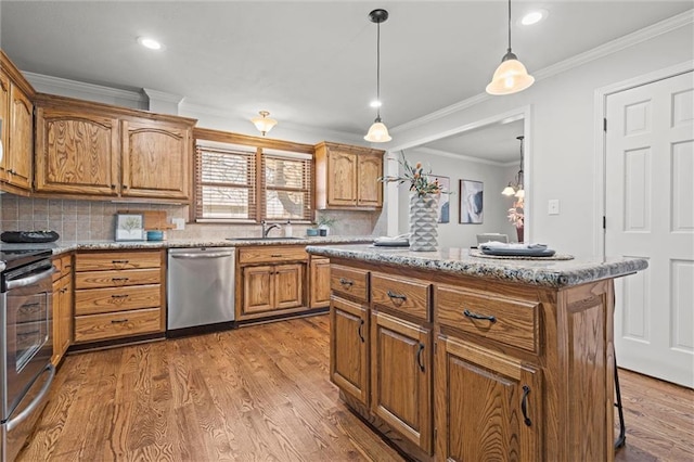 kitchen featuring crown molding, decorative light fixtures, appliances with stainless steel finishes, wood finished floors, and a sink