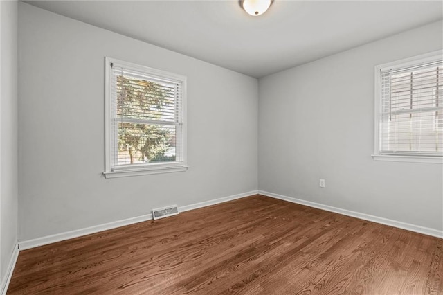 unfurnished room featuring dark wood-style floors, visible vents, and baseboards