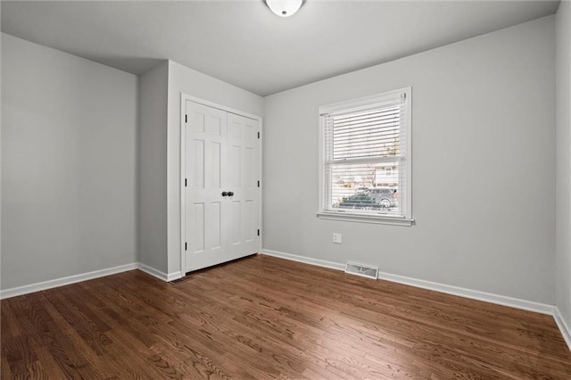 unfurnished bedroom with visible vents, dark wood-style floors, baseboards, and a closet