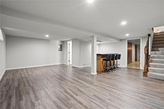 finished basement with stairway, baseboards, a bar, and wood finished floors