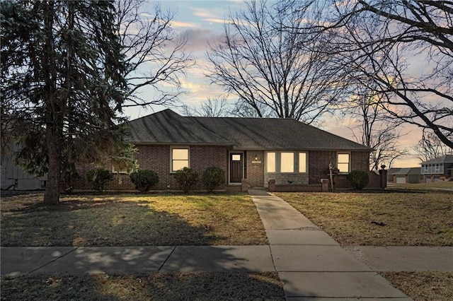 ranch-style house with brick siding, a lawn, and a shingled roof