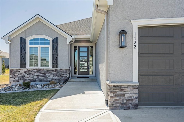 doorway to property with stone siding, stucco siding, a shingled roof, and a garage