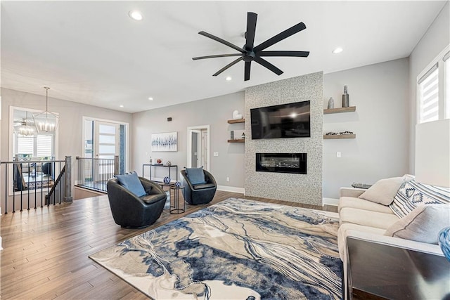 living area featuring ceiling fan with notable chandelier, wood finished floors, recessed lighting, a fireplace, and baseboards