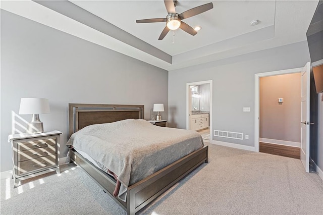 carpeted bedroom with ensuite bath, a raised ceiling, baseboards, and visible vents