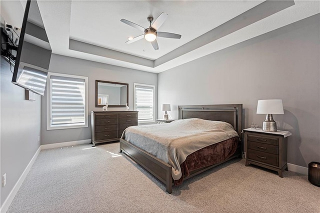 bedroom with baseboards, a raised ceiling, and light carpet