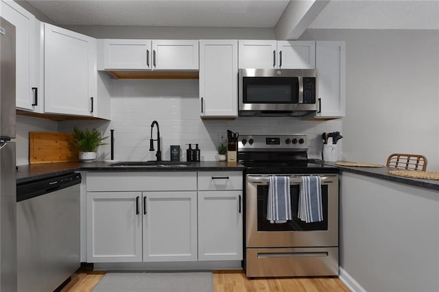 kitchen featuring backsplash, stainless steel appliances, light wood-style floors, white cabinetry, and a sink