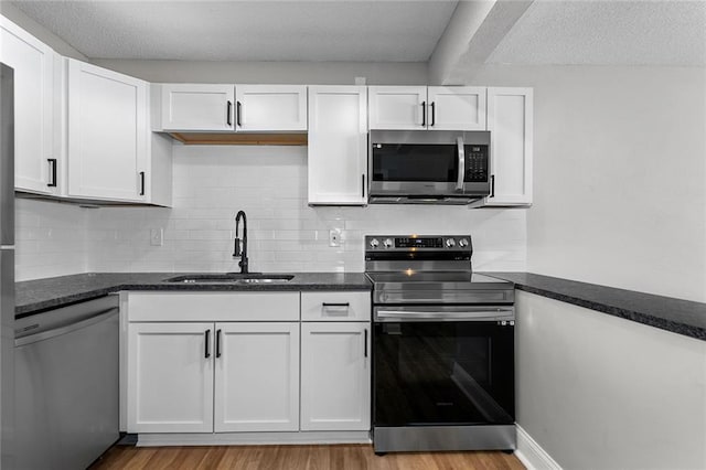 kitchen featuring a sink, backsplash, wood finished floors, white cabinetry, and appliances with stainless steel finishes