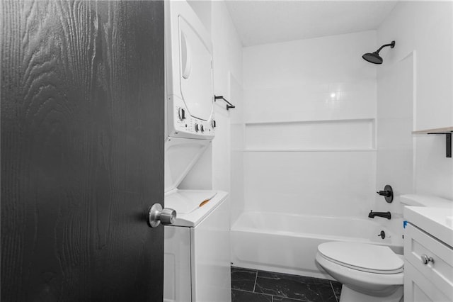 bathroom featuring stacked washer / dryer, toilet, bathtub / shower combination, marble finish floor, and vanity